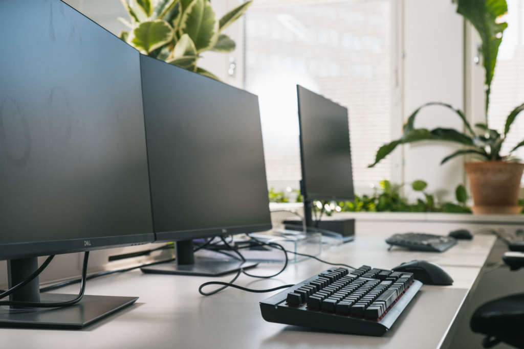 Työpöytä toimistolla, jossa näkyy kolme näyttöä.